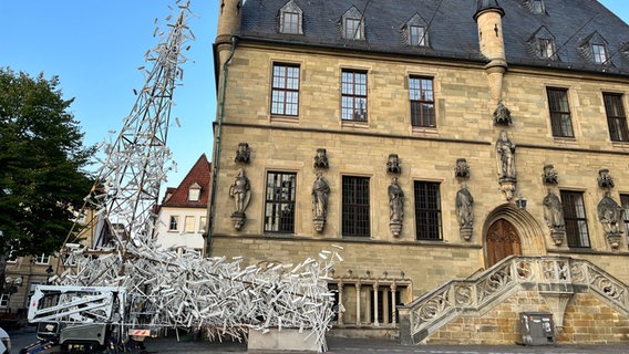 Weiß lackierte Mistgabel, deren Zinken in Holzscheiten stecken sind für ein Kunstwerk an einem Stahlgerüst befestigt. © NDR Foto: Carsten Ehrbar