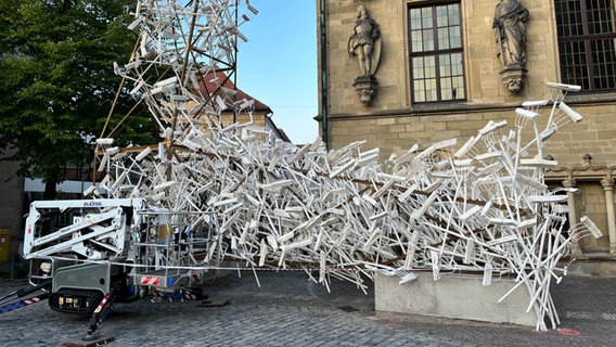 Weiß lackierte Mistgabel, deren Zinken in Holzscheiten stecken sind für ein Kunstwerk an einem Stahlgerüst befestigt. © NDR Foto: Carsten Ehrbar