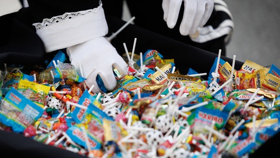 Ein Karnevalist mit weißen Handschuhen greift in einen Behälter mit Süßigkeiten beim 46. traditionellen Karnevalsumzug "Ossensamstag". © dpa-Bildfunk Foto: Friso Gentsch