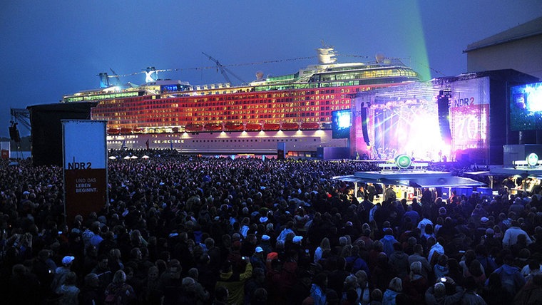 Vor dem farbig beleuchteten Kreuzfahrtschiff-Neubau "Celebrity Silhouette" an der Ausrüstungspier der Meyer-Werft, tritt die deutsche Rockgruppe "The Scorpions" auf der NDR 2 Festivalbühne auf. © dpa Fotograf: Ingo Wagner