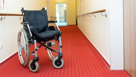 Auf einem Flur in einem Seinorenheim steht ein Rollstuhl vor der Zimmertür eine Bewohnerin. © picture alliance/Fotostand/Gelhot Foto: Fotostand/Gelhot