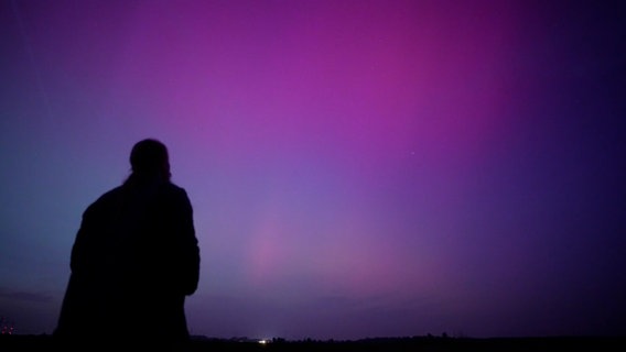 Die Silhouette eines Mannes, der Polarlichter der Farbe Magenta beobachtet. © Nord-West-Media TV 