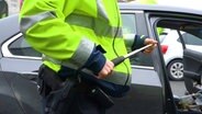 Ein Polizist mit einem beschlagnahmten Schlagstock auf einem Autobahnparkplatz. © Nord-West-Media TV 