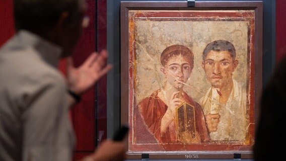 Ein Mann schaut sich ein Gemälde an, das Menschen aus Pompeji zeigt. © dpa Foto: Friso Gentsch