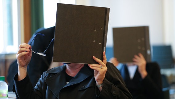 Zwei Angeklagte verdecken ihr Gesicht mit einem Aktenordner in einem Saal vom Landgericht Osnabrück. © dpa-Bildfunk Foto: Friso Gentsch/dpa