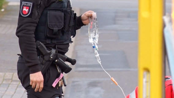Eine Polizistin hält einen Infusionsbeutel während ein verletzter Radfahrer versorgt wird. © Nord-West-Media TV 