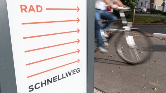 Auf einem Schild steht Radschnellweg; im Hintergrund fährt ein Fahrrad vorbei. © dpa - Bildfunk Foto: Friso Gentsch