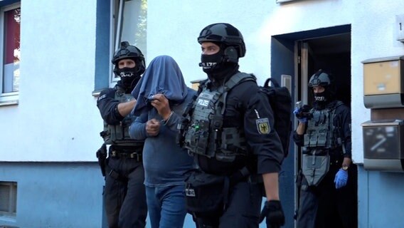 Ein Mann wird in Osnabrück von Polizisten in Schutzkleidung abgeführt. © TV7NEWS 