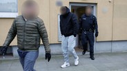Beamte der Polizei führen einen Beschuldigten aus einem Haus ab. © dpa Foto: Friso Gentsch
