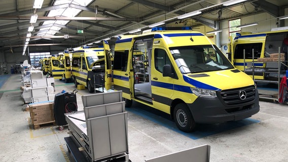 Blau-gelbe Rettungswagen stehen in einer Fertigungshalle. © NDR Foto: Hedwig Ahrens