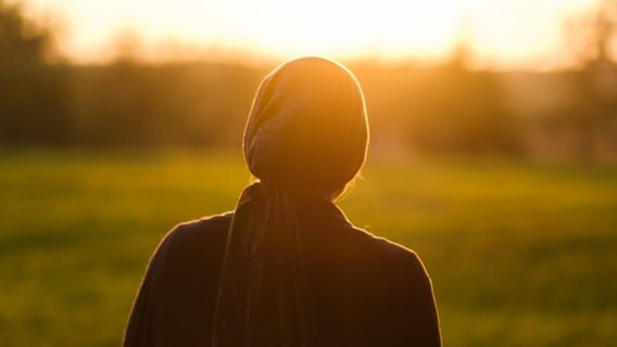 Ein Frau steht bei Sonnenuntergang auf einer Wiese. © picture alliance Foto: Ole Spata