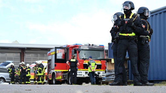 Drei Polizisten stehen in einem Dreieck zusammen - im Hintergrund sind ein Feuerwehrauto und Einsatzkräfte der Feuerwehr zu sehen. © picture alliance/dpa Foto: Lars Penning/dpa