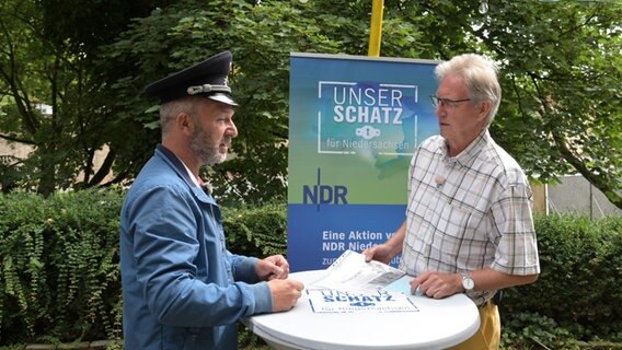 Ein NDR Moderator steht mit einem Mann an einem Stehtisch und trägt eine Polizeimütze. © NDR Foto: Michael Bahlo