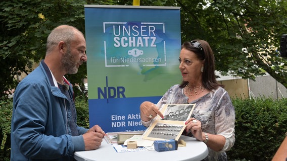 Ein NDR-Moderator lässt sich von einer Frau alte schwarz/weiß Fotos zeigen. © NDR Foto: Michael Bahlo