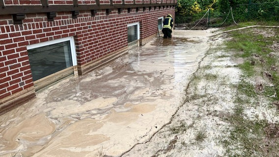 Ein Feuerwehrmann pumpt Regenwasser aus einer Grube an einem Wohnhaus in Georgsmarienhütte. © dpa Bildfunk Foto: Torben Kipp/Nord-West-Media/dpa