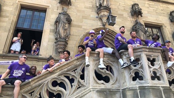 Zur Feier des Aufstiegs des VfL Osnabrück sitzen und stehen Mitglieder der Entourage der Mannschaft mit Trikots am Rathaus. © NDR Foto: Marlena Maerz