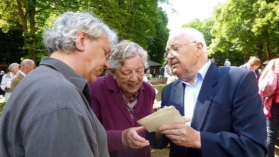 Drei Personen schauen alte schwarz-weiß Aufnahmen an. © NDR Foto: Hedwig Ahrens