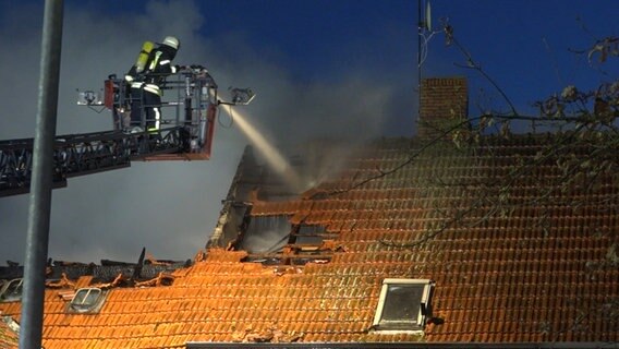 Eine Einsatzkraft der Feuerwehr löscht einen Brand in einem Wohnhaus von einer Drehleiter aus. © Nord-West-Media TV 
