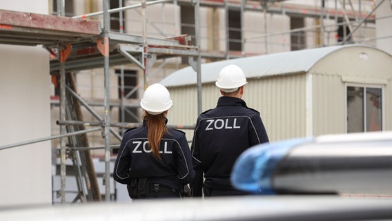 Eine Zollbeamtin und ein Zollbeamter von hinten gesehen laufen über eine Baustelle. Eine Zollbeamtin und ein Zollbeamter von hinten gesehen laufen über eine Baustelle. © Hauptzollamt Osnabrück