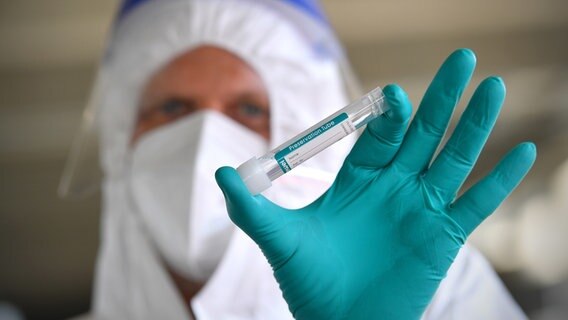 Ein Mensch in Schutzkleidung hält ein Röhrchen mit Abstrichen für einen PCR-Test. © picture alliance Foto: picture alliance / SVEN SIMON | Frank Hoermann / SVEN SIMON