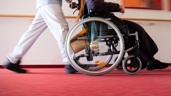 Ein Pfleger eines Pflegeheims schiebt eine Bewohnerin in einem Rollstuhl. (Archivbild) © dpa-Bildfunk Foto: Tom Weller