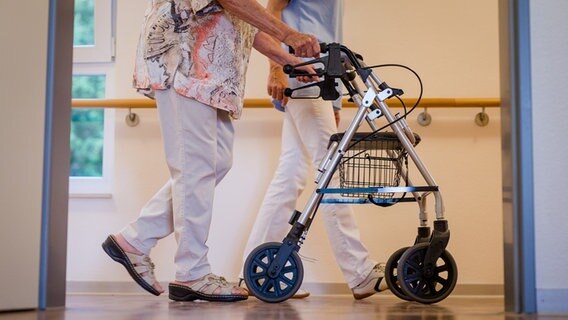 Eine Pflegekraft läuft mit einer alten Dame über einen Gang in einem Pflegeheim. © dpa-Bildfunk Foto: Christoph Schmidt