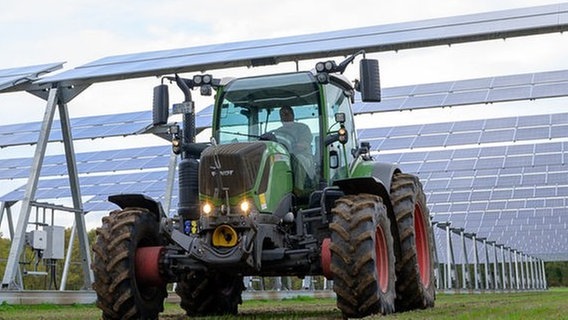 Ein Landwirt fährt mit einem Trecker unterhalb einer Agrar-Photovoltaik-Anlage entlang. © dpa-Bildfunk Foto: Philipp Schulze/dpa