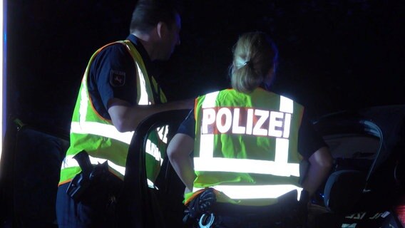 Zwei Einsatzkräfte der Polizei stehen bei Nacht an einem Unfallsort und tragen Warnwesten mit der Aufschrift "Polizei". © TeleNewsNetwork 