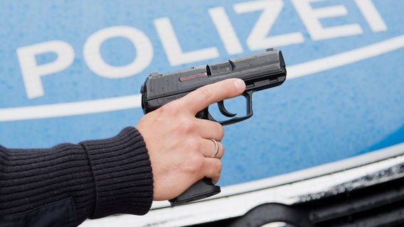 Ein Polizist posiert für Fotoaufnahmen mit seiner Dienstwaffe HK P2000 9mm vor einem Polizeifahrzeug. © dpa-Bildfunk Foto: Julian Stratenschulte