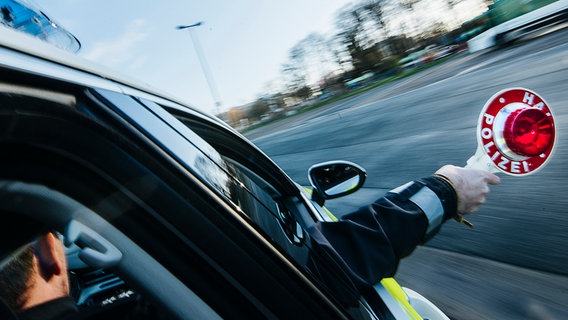 Ein Polizist hält eine rote Polizeikelle aus dem Beifahrerfenster eines Streifenwagens.  © NDR Foto: Julius Matuschik