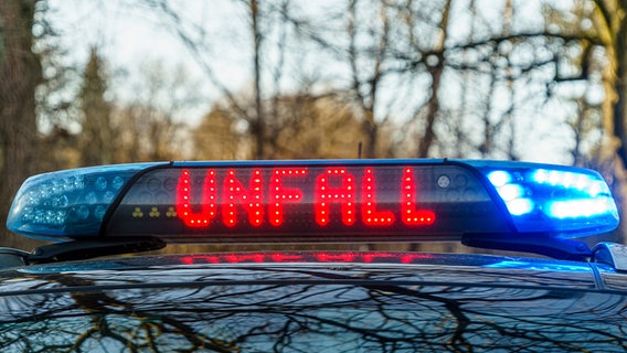Auf einer Strasse steht ein Einsatzfahrzeug der Polizei mit Blaulicht und dem Schriftzug Unfall bei einem Verkehrsunfall. © picture alliance Foto: Reiß