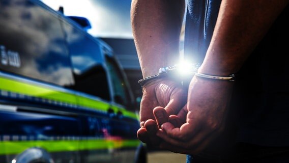 Ein Mann in Handschellen steht neben einem Polizeifahrzeug. © picture alliance/Fotostand/K. Schmitt Foto: K. Schmitt