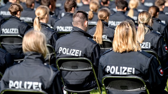 Polizistinnen und Polizisten des Bachelorstudienjahrgangs der Polizeiakademie Niedersachsen sitzen bei ihrer Abschlussfeier auf einem Sportplatz. © picture alliance/dpa/Hauke-Christian Dittrich Foto: Hauke-Christian Dittrich