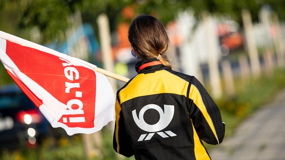 Eine Beschäftigte der Deutschen Post steht mit einer Fahne der Gewerkschaft Verdi vor der Deutsche-Post-DHL-Niederlassung im Stadtteil Anderten. © picture alliance/dpa | Moritz Frankenberg Foto: Moritz Frankenberg