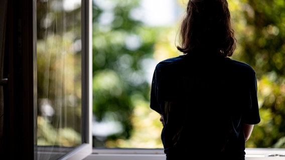 Eine Frau steht in ihrer Wohnung an einem Fenster. © picture alliance/dpa Foto: Fabian Sommer