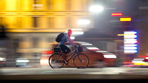 Eine Radfahrerin fährt bei Nacht durch eine Stadt. © dpa picture-alliance Foto: Christian Charisius
