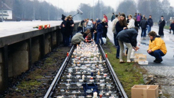 Viele Menschen stehen vor Bahnschienen, auf denen Kerzen aufgebaut sind. © NDR 
