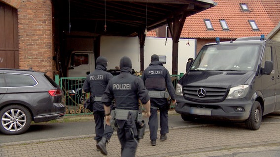 Spezialeinsatzkräfte der Polizei stehen mit zwei Einsatzfahrzeugen für eine Razzia zu Reichsbürgern vor einem Hof. © NDR 
