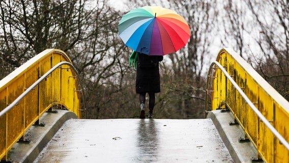 Eine Frau geht mit einem bunten Regenschirm über eine Brücke. © dpa-Bildfunk Foto: Friso Gentsch/dpa