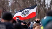 Teilnehmer auf einer Demonstration von Rechtsextremen und Reichsbürgern halten eine Fahne, die an die Reichsflagge erinnert. © picture alliance/Geisler-Fotopress Foto: Jean MW/Geisler-Fotopress