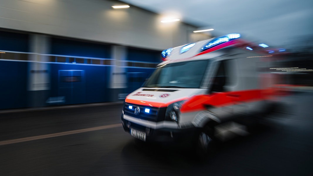 Ein mit Bewegungsunschärfe fotografierter Rettungswagen fährt mit Blaulicht über eine Straße.