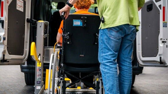 Eine Frau in einem Rollstuhl wird in ein Taxi geschoben. © picture alliance / ANP | ROB ENGELAAR 