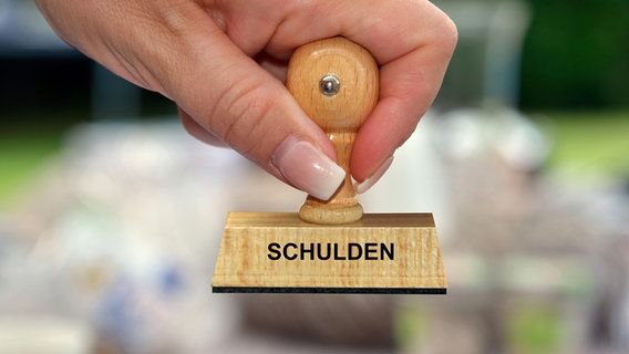 Eine Person hält einen Holzstempel mit der Aufschrift "Schulden" in der Hand. © picture alliance/Bildagentur-online/McPhoto 