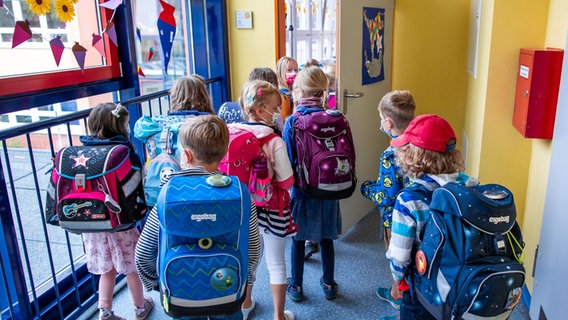 Mehrere Grundschüler gehen durch einen Schulflur auf ein Klassenzimmer zu. © picture alliance/dpa Foto: Jens Büttner