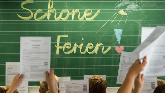 Schüler halten in einem Klassenzimmer ihre Zeugnisse hoch. Im Hintergrund steht auf einer Tafel "Schöne Ferien". © picture-alliance/dpa Foto: Armin Weigel