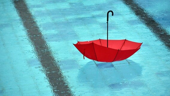 Ein roter Regenschirm schwimmt in einem Schwimmbad. © picture alliance / ZB Foto: Ralf Hirschberger