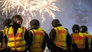 Polizisten in Schutzausrüstung stehen unter einem Silvester-Feuerwerks-Himmel. © picture alliance/dpa | Clemens Heidrich Foto: Clemens Heidrich