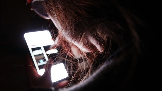A person looks at a brightly lit smartphone display, the room is dark.  © picture alliance/dpa Photo: Weronika Peneshko
