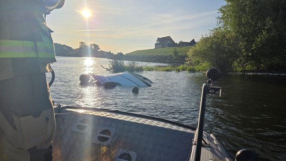 Ein Feuerwehrmann auf einem Boot nähert sich einer Bugspitze eines Sportbootes, die aus dem Wasser der Elbe ragt. © Feuerwehr Samtgemeinde Elbmarsch Foto: Feuerwehr Samtgemeinde Elbmarsch