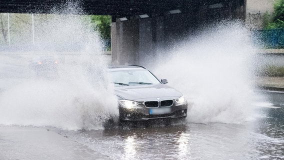 Ein Auto fährt über eine von Starkregen überflutete Straße. © picture alliance / Julian Stratenschulte/dpa | Julian Stratenschulte 